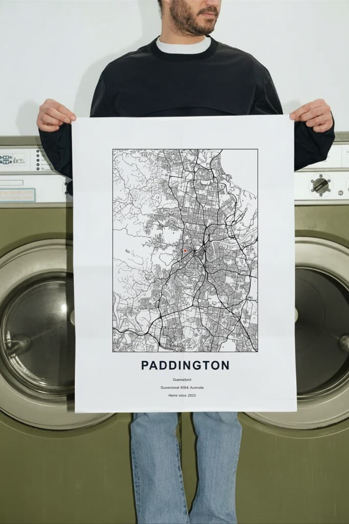 Map poster held in front of olive-toned washers: minimal street map with place name and detail lines.